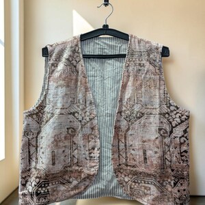 Puede incluir: Un chaleco sin mangas con un exterior estampado en tonos rosa y marrón apagados con un diseño geométrico. El forro interior es visible, mostrando un patrón de rayas verticales finas en gris claro y blanco. La prenda cuelga de una percha negra.