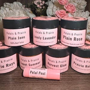 May include: Seven black jars with pink labels featuring the brand name Petals & Prairie and various product names including Plain Jane, Lovely Lavender, Plain Rose, Prairie Rays, Sweet Summer, Harvest Glow, and Prairie Relief, plus a lip balm.