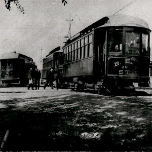 Peut inclure: Une photographie en noir et blanc montrant deux tramways électriques anciens sur des rails. Le tramway avant porte l'inscription B. E. 20 ST sur son panneau frontal. Plusieurs silhouettes se tiennent près des voies dans cette scène historique.