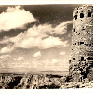 Peut inclure: Une photographie vintage en noir et blanc d'une haute tour cylindrique en pierre avec plusieurs ouvertures de fenêtres carrées, située au bord d'un canyon profond aux formations rocheuses stratifiées sous un ciel nuageux. Texte : SF110.