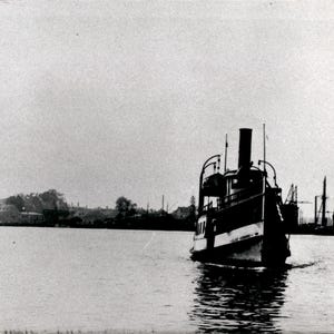 Peut inclure: Une photographie en noir et blanc d'un bateau à vapeur ancien naviguant sur une eau calme. Le navire présente une cheminée centrale proéminente, une structure de cabine à plusieurs niveaux et le texte "CLYDE HERRING" visible sur la coque.