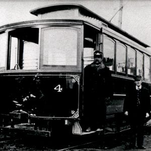 Peut inclure: Une photographie vintage en noir et blanc d'un tramway marqué du numéro 4 sur son panneau avant. Le tramway présente de grandes fenêtres sur le côté et une section de toit surélevée. Deux personnes en uniforme sombre se tiennent près de l'entrée.