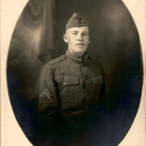Peut inclure: Un portrait vintage en noir et blanc d'un soldat portant un uniforme militaire en laine avec un col haut, des poches boutonnées et un insigne de grade en chevron sur la manche. Le soldat porte une calot avec un petit emblème circulaire.
