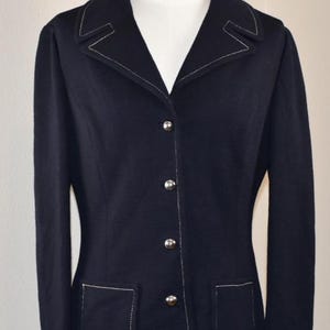 Può includere: Un blazer blu navy scuro con impunture bianche a contrasto lungo i revers, l'abbottonatura frontale, i polsini e due tasche applicate. La giacca è chiusa da quattro bottoni argentati lucidi sul davanti e presenta maniche lunghe.