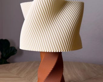 May include: A table lamp featuring a textured, off-white, wavy lampshade with a repeating dot pattern, supported by a cylindrical, rust-colored base with a spiraling, geometric, three-dimensional grid texture that matches the shade's pattern.
