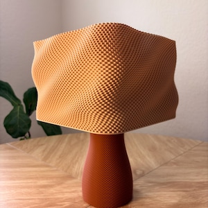 May include: A 3D printed object featuring a light orange, wavy, square-shaped top section with a textured grid pattern, supported by a solid, darker reddish-brown cylindrical base that also displays a fine, uniform grid texture throughout.