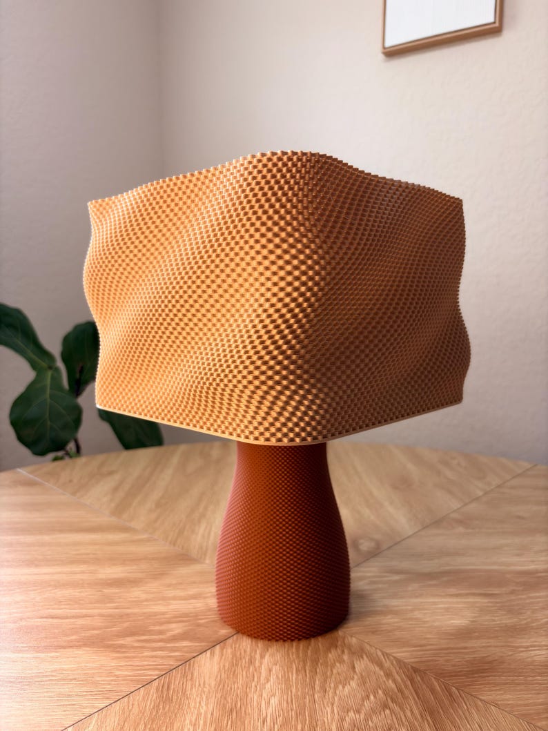 May include: A 3D printed object featuring a light orange, wavy, square-shaped top section with a textured grid pattern, supported by a solid, darker reddish-brown cylindrical base that also displays a fine, uniform grid texture throughout.