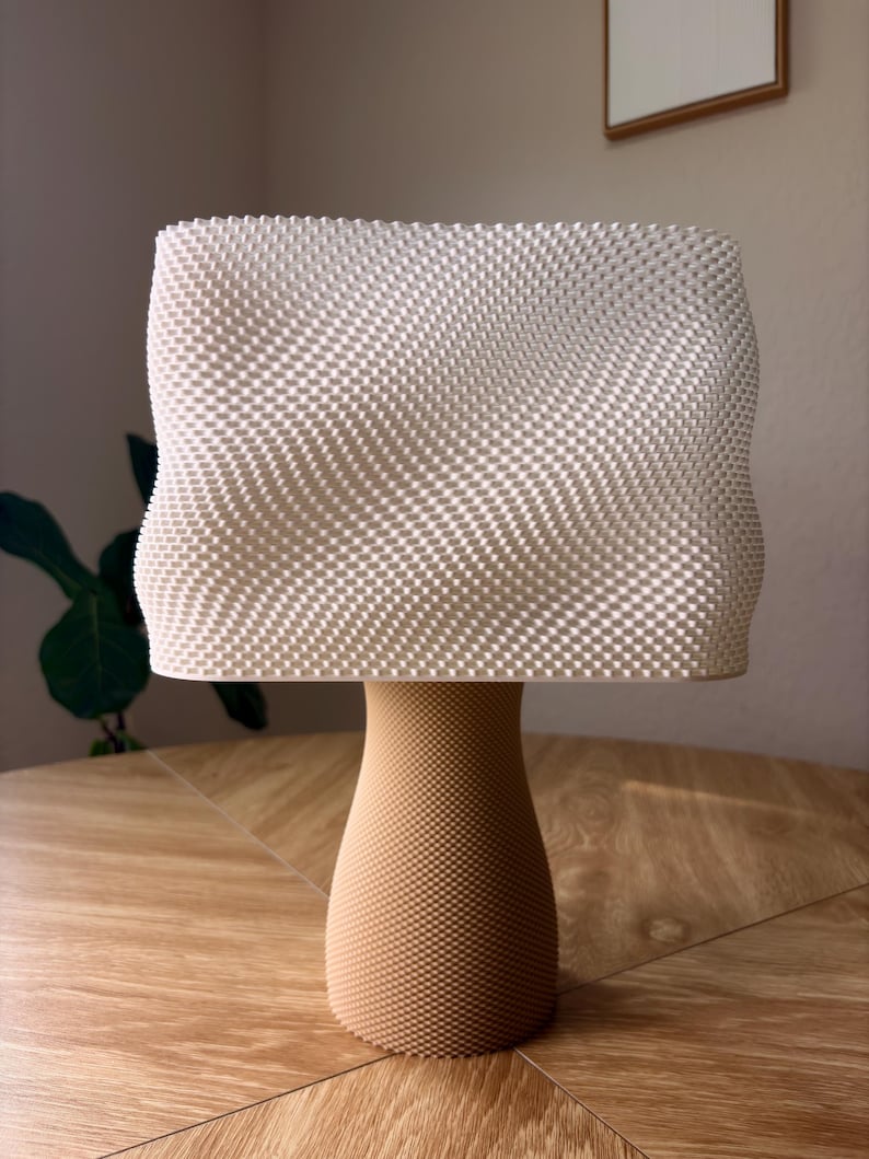 May include: A table lamp featuring a rectangular, off-white lampshade with a textured, grid-like surface pattern. The base is a tan, cylindrical pedestal with a tapered middle section, also displaying a fine, uniform, textured grid pattern.