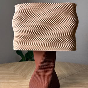 May include: A table lamp featuring a rectangular, light beige lampshade with a fine, grid-like textured surface. The base is a dark reddish-brown, twisted, square-shaped column with a matching fine, grid-like textured pattern throughout.