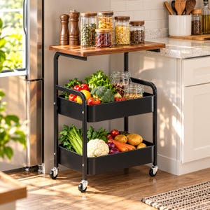 May include: A two-tier black metal rolling cart with a wooden top shelf. The cart features four caster wheels and two deep storage baskets filled with fresh produce including broccoli, cauliflower, carrots, potatoes, and peppers.