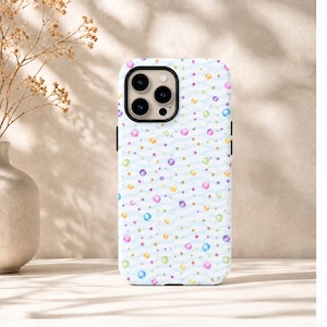 May include: A smartphone case featuring a light blue wavy line pattern across a white background. The design is decorated with small, colorful spheres in shades of pink, purple, yellow, and green, interspersed with tiny gold-colored stars.