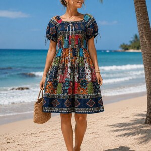 Puede incluir: Un vestido hasta la rodilla con base azul oscuro y un patrón de patchwork multicolor con motivos geométricos y florales. El vestido tiene mangas cortas abullonadas con lazos, un escote cuadrado con cordón y un cuerpo fruncido.