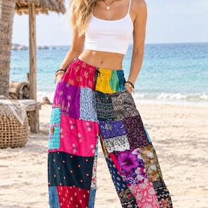 May include: A white spaghetti strap crop top paired with loose-fitting, high-waisted patchwork trousers. The trousers feature a vibrant, multi-coloured design with various floral, geometric, and paisley patterns in shades of pink, yellow, blue, and purple.