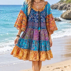 May include: A tiered knee-length dress featuring a vibrant mix of blue, purple, and orange paisley and floral patterns. The garment has a scoop neckline with a drawstring tie, three-quarter length bell sleeves, and a ruffled hemline design.