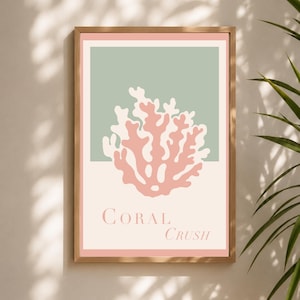 Puede incluir: Una lámina de arte mural enmarcada con una ilustración de coral estilizada en rosa suave sobre un fondo verde salvia y crema. El texto 'CORAL CRUSH' está impreso en una fuente serif en la parte inferior de la lámina, dentro de un marco de madera clara.