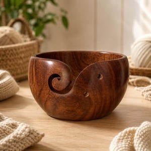 Peut inclure: Un bol à laine en bois brun foncé avec une finition lisse et polie et un grain de bois visible. Le bol présente une découpe en spirale caractéristique sur le côté pour guider le fil, ainsi que deux petits trous circulaires pour le rangement.