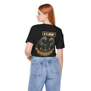 May include: A black short-sleeve t-shirt featuring a graphic on the back with the text U.S. ARMY in a yellow box above a ram head, three skulls wearing helmets, and a banner with the text Killing Is Our Business And Business Is Great.