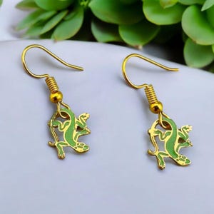 May include: A pair of gold earrings with green lizard charms. The lizards are detailed with gold outlines and green enamel.