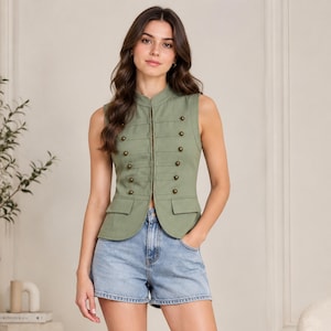 Può includere: Un gilet senza maniche verde oliva con colletto alla coreana, chiusura frontale con gancetti e due file di bottoni decorativi color ottone. Il capo presenta due tasche frontali con patta e una vestibilità strutturata e aderente.
