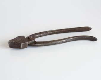 May include: A vintage rusty metal tool with two curved arms and a pointed jaw. The tool is designed for gripping and pulling objects.