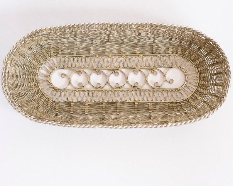 May include: A silver wire basket with a decorative design. The basket is oval shaped and has a woven pattern.
