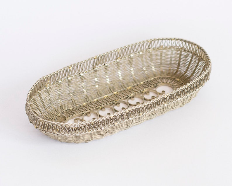 May include: A silver wire basket with an oval shape and decorative details. The basket is made of thin wire and has a delicate, intricate design.