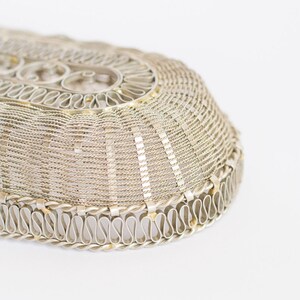 May include: A silver oval-shaped wire basket with a decorative woven pattern. The basket has a scalloped edge with a repeating S-shaped design.