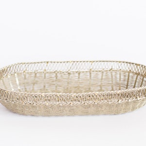 May include: A silver oval-shaped wire basket with a decorative woven pattern. The basket is made of thin wire and has a delicate, intricate design.
