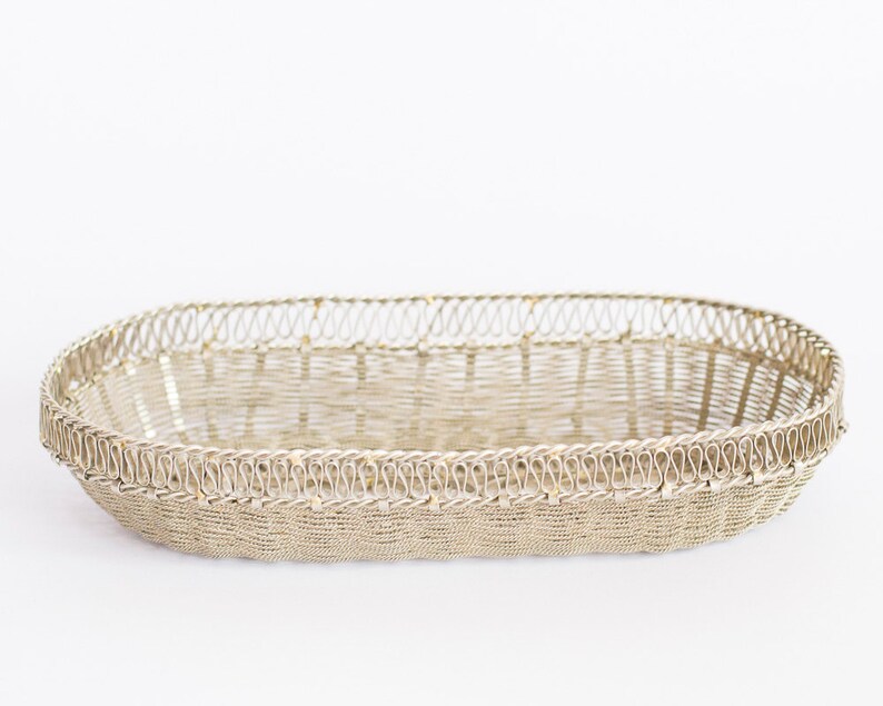 May include: A silver oval-shaped wire basket with a decorative woven pattern. The basket is made of thin wire and has a delicate, intricate design.