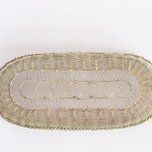 May include: A silver oval-shaped wire basket with a decorative design. The basket has a woven wire pattern and a scalloped edge.