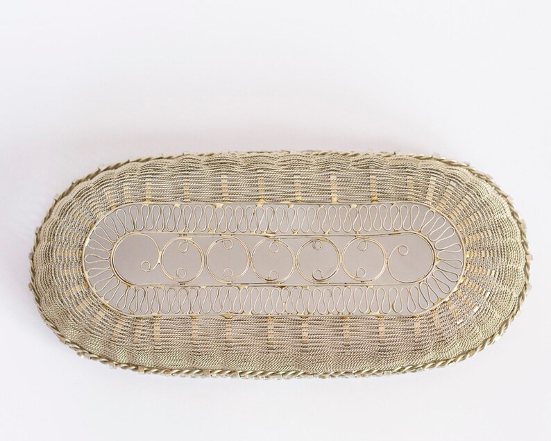 May include: A silver oval-shaped wire basket with a decorative design. The basket has a woven wire pattern and a scalloped edge.