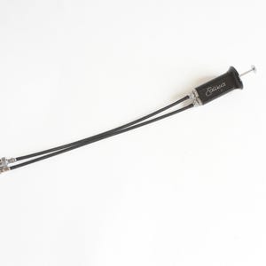 May include: A black camera cable release with the word "Edixa" in cursive script. The release has a silver-coloured plunger and two black cables with silver-coloured connectors. The item is set against a white background.