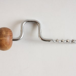 Può includere: Un cavatappi argentato con un manico in legno. Il cavatappi ha una lama lunga e a spirale e un manico curvo.
