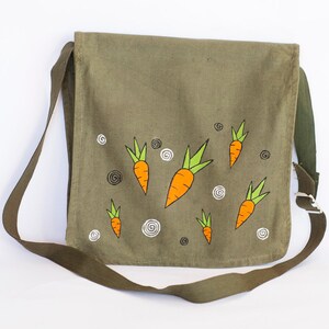 May include: A green canvas messenger bag with a shoulder strap. The bag has a whimsical design featuring multiple orange carrots with green tops.