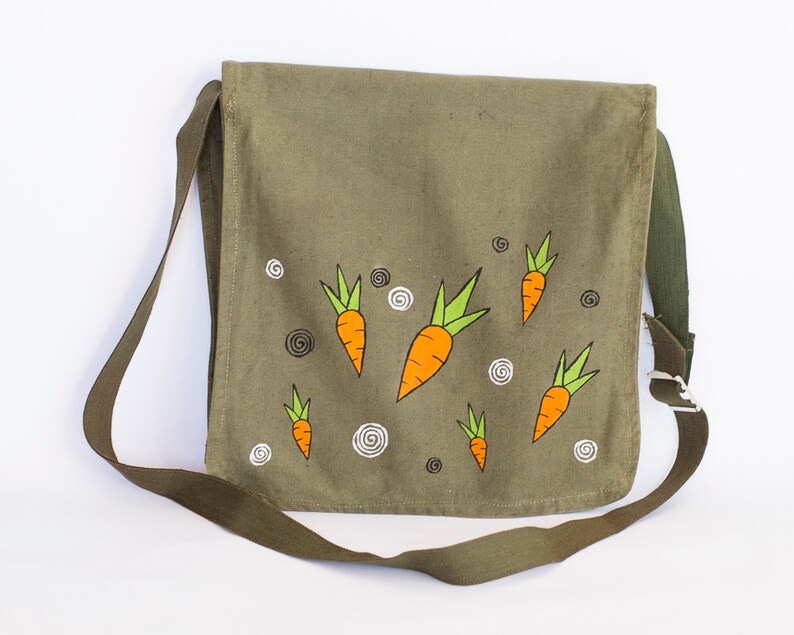 May include: A green canvas messenger bag with a shoulder strap. The bag has a whimsical design featuring multiple orange carrots with green tops.
