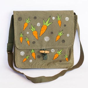 May include: A green canvas messenger bag with a brown leather strap and a wooden toggle closure. The bag is decorated with hand-painted orange carrots with green tops.