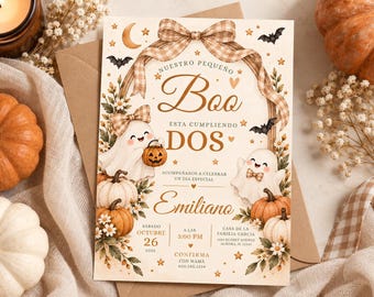Puede incluir: Una tarjeta de invitación rectangular con fondo beige, ilustrada con dos fantasmas sonrientes, calabazas, murciélagos, estrellas y un lazo de cuadros. El texto dice: NUESTRO PEQUEÑO Boo ESTA CUMPLIENDO DOS, EMILIANO, SÁBADO OCTUBRE 26, 3:00 PM, CASA DE LA FAMILIA GARCIA.