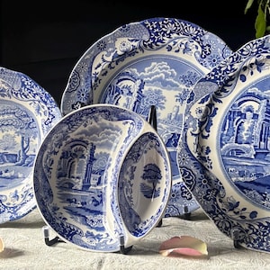 May include: A collection of blue and white ceramic dinnerware featuring a detailed transferware landscape pattern. The set includes an oval platter, a round divided dish, and a large round plate, all with scalloped edges and intricate floral borders.