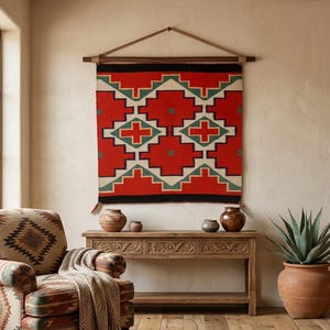 Peut inclure: Une tenture murale tissée rectangulaire présentant un motif géométrique rouge, crème et bleu sarcelle, suspendue à une tringle en bois foncé avec une lanière en cuir. Le textile affiche un motif répétitif de croix et de losanges avec des bordures noires.