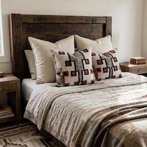 May include: A rustic dark wood headboard paired with a bed featuring a light beige linen duvet, two large solid beige pillows, and two square accent pillows decorated with a repeating geometric pattern in dark gray and deep red tones.