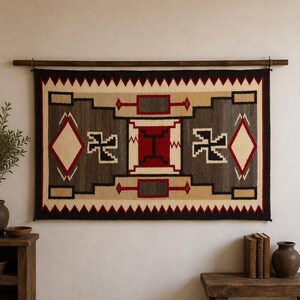 Peut inclure: Une tenture murale tissée rectangulaire présentant un motif géométrique dans des tons crème, gris anthracite, noir et rouge profond. Le design comprend des blocs rectangulaires centraux, des losanges et des motifs en escalier, suspendus à une tringle en bois sombre.