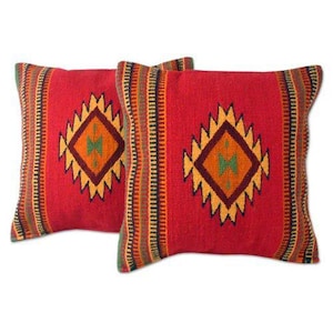 May include: Two square throw pillows featuring a vibrant red base color. Each pillow displays a central diamond-shaped geometric pattern in yellow, orange, and dark brown, flanked by vertical striped bands in green, yellow, and dark brown.