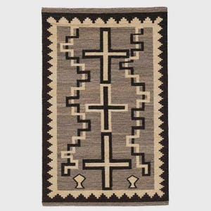 Peut inclure: Un tapis tissé rectangulaire présentant une colonne centrale verticale de trois croix noires sur un fond gris. Le motif comprend une bordure géométrique en escalier, dentelée en noir et crème, encadrant le motif central symétrique.
