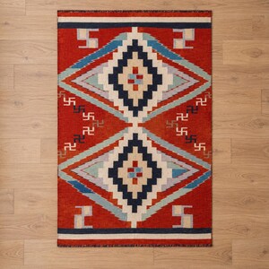 May include: A rectangular area rug featuring a vibrant red background with two large, centered diamond patterns in navy blue, light blue, and cream. The design includes small, repeating geometric symbols in navy and cream throughout the field.