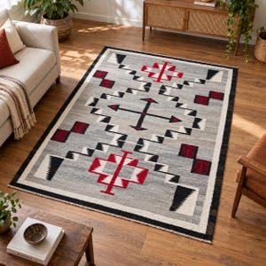 Peut inclure: Un tapis rectangulaire au fond gris orné d'un motif géométrique noir, blanc et rouge. Le design présente des formes en losange à degrés, des motifs en forme de flèche et de petits carrés à damier, le tout encadré par une bordure noire.