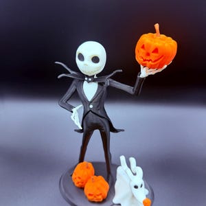 May include: A figurine of a tall, slender character with a white skull-like head wearing a black suit, holding an orange jack-o'-lantern. Two smaller orange pumpkins and a white ghost-like dog figure stand on the base at the character's feet.