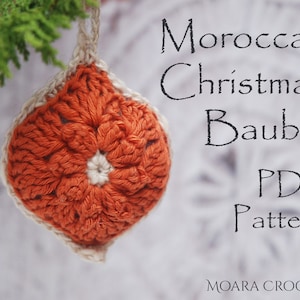 May include: A crocheted orange and white Christmas ornament in the shape of a flower, hanging from a green branch. The text "Moroccan Christmas Bauble PDF Pattern" is written in black on a white background.