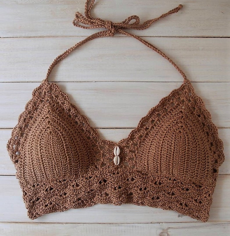 Pu&ograve; includere: Un top halter in crochet marrone con un accento a conchiglia al centro. Il top ha un bordo a festoni e una chiusura a cravatta sul collo.