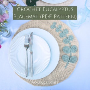 Può includere: Tovaglietta all'uncinetto Eucalipto (schema PDF) - Primo piano di una tovaglietta all'uncinetto beige con un motivo a foglia di eucalipto verde. Un piatto bianco con una forchetta e un coltello d'argento è sopra la tovaglietta.