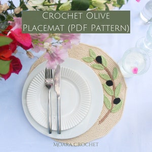 Puede incluir: Patrón de mantel individual de crochet de oliva en PDF. Un mantel individual de crochet beige con un diseño de rama de olivo verde. El mantel individual está sobre un mantel blanco con un plato blanco y cubiertos encima.